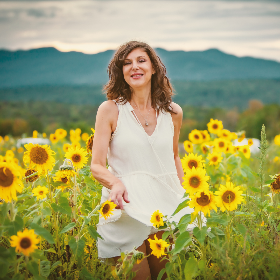 Femme de 50 ans avec une peau jeune dans un champ de magnifiques tournesols, une fleur dont huile est gorgée d'antioxydant, aux multiples autres propriétés pour la peau.