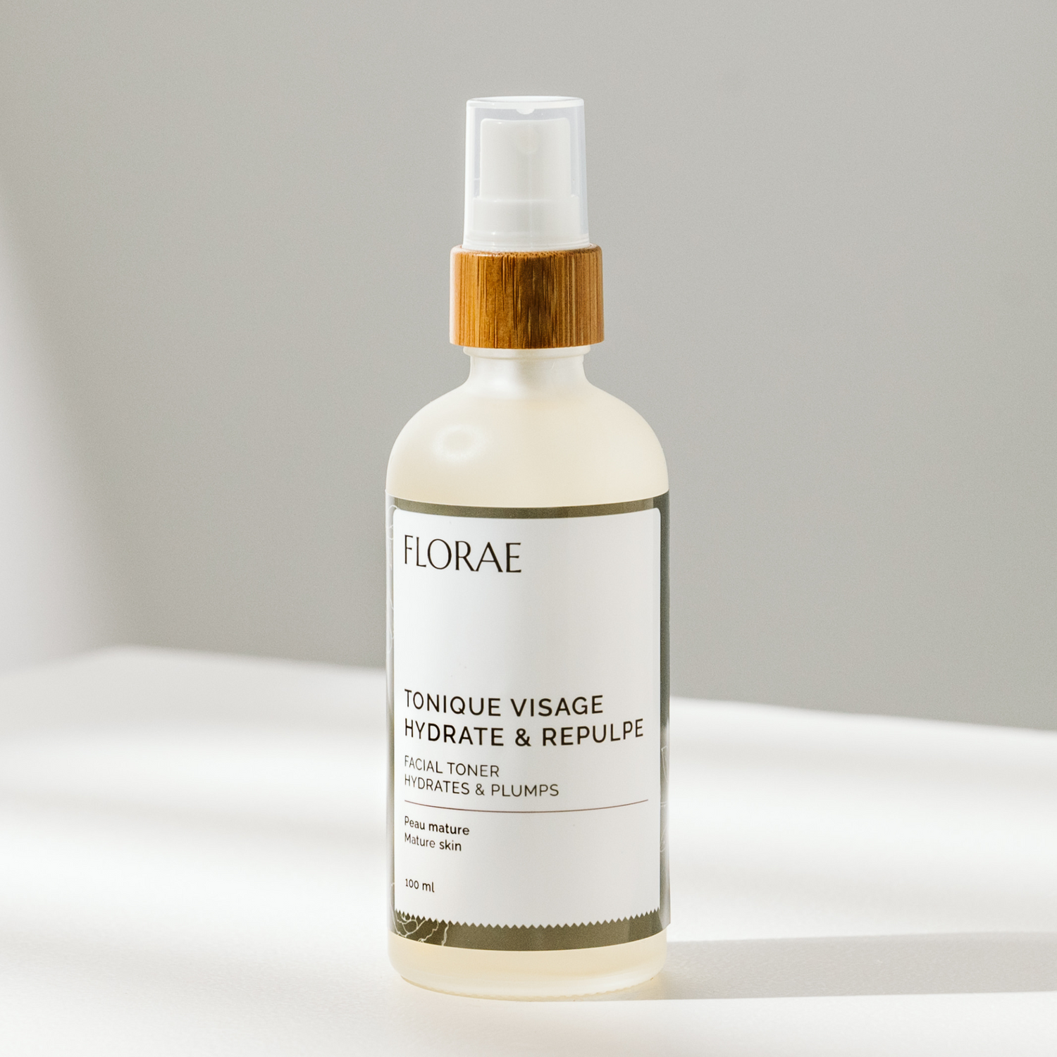 onique pour le visage de la gamme Florae cosmétiques. Présenté dans une bouteille de verre avec un bouchon de bambou vaporisateur, sur un fond blanc.